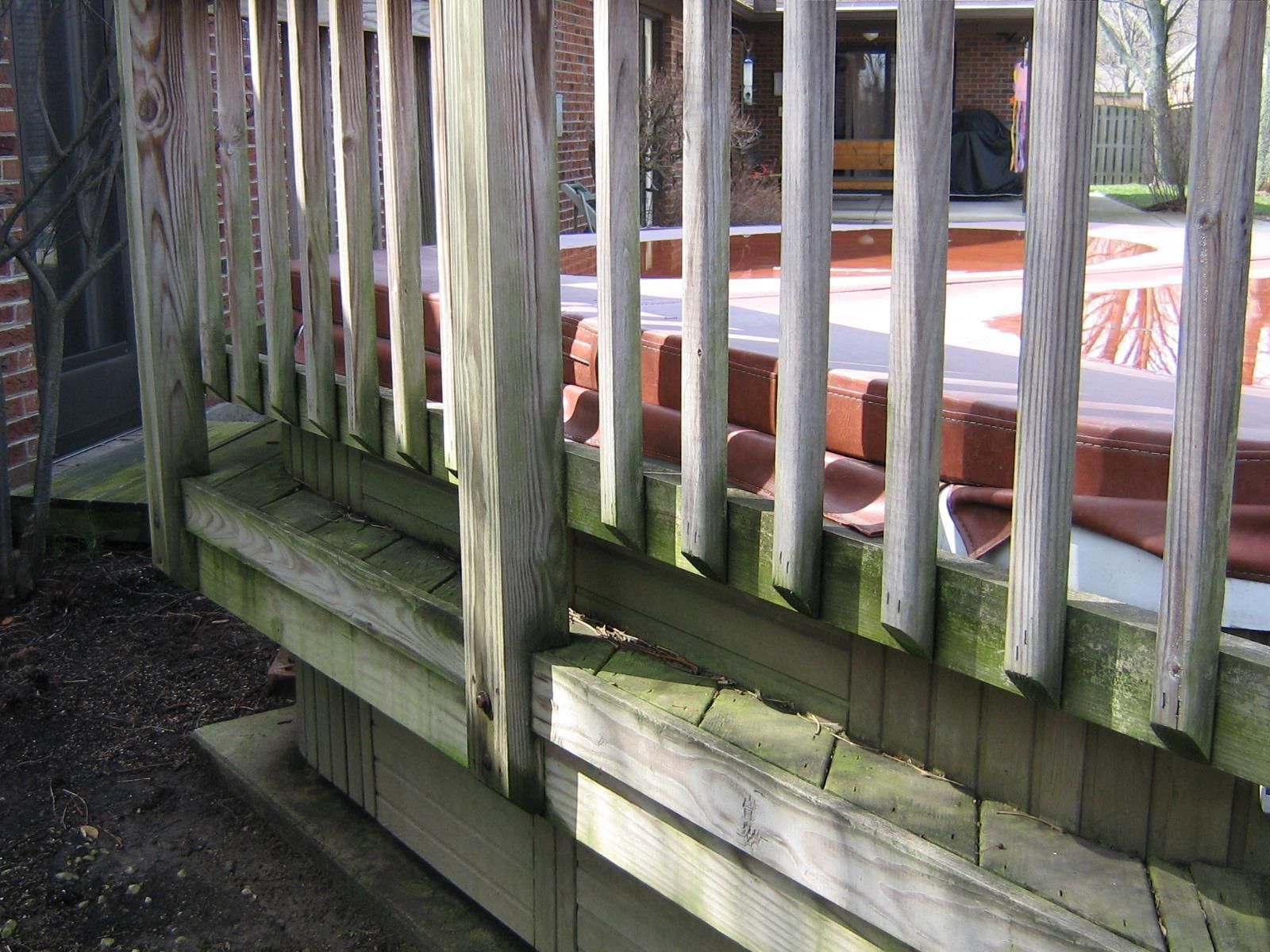A wooden deck railing surrounds a hot tub covered with a brown thermal lid on a residential patio.