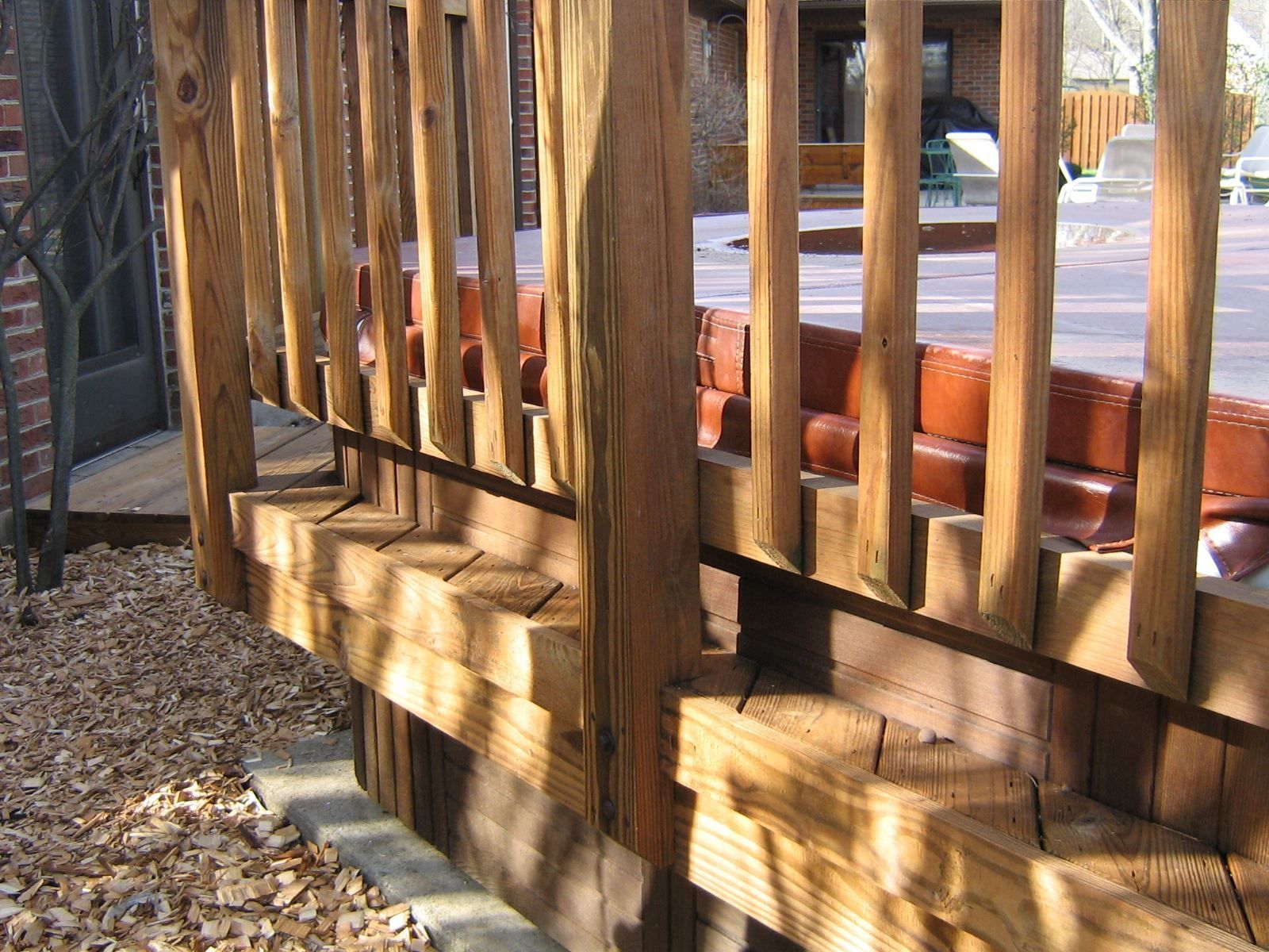 A close-up view of a wooden deck with vertical railings, showing structural support beams above a gravel ground surface.