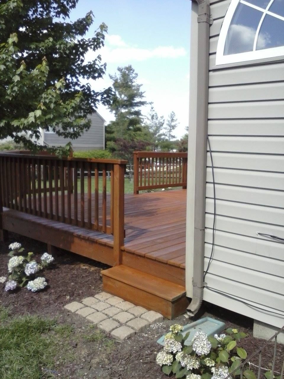A wooden deck with railings extends from the side of a light-colored house, featuring a short staircase to the ground.