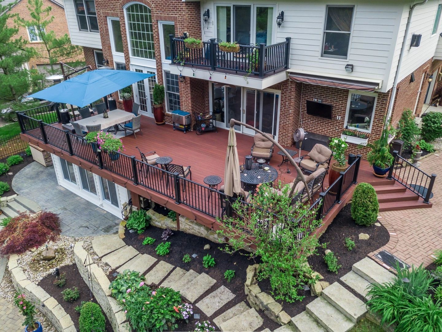 An elevated wooden deck with outdoor seating, a blue umbrella, and a balcony, overlooking a stone-landscaped backyard.