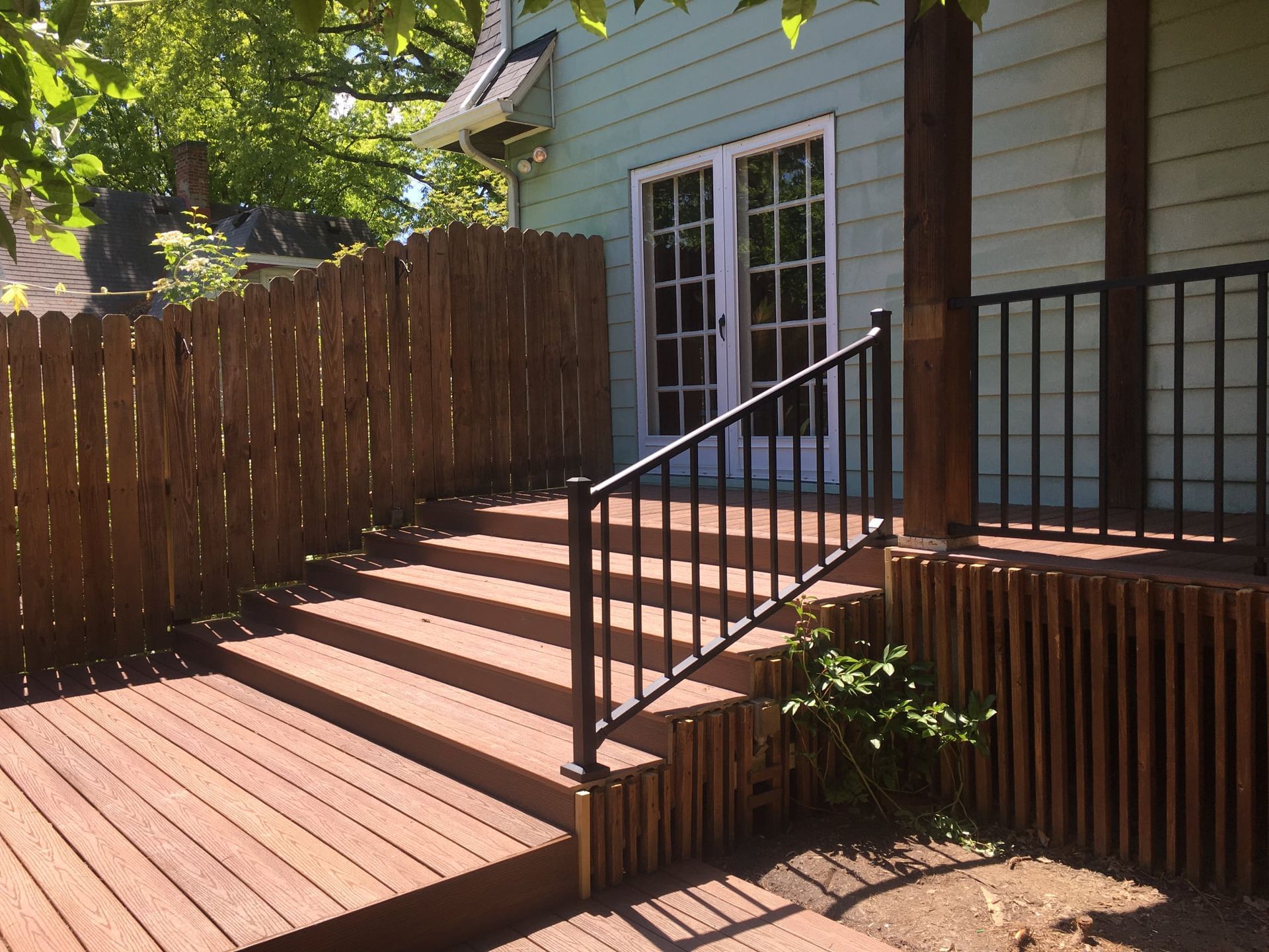 Wooden deck steps with a black metal railing leading to a light green house with white-framed French doors.