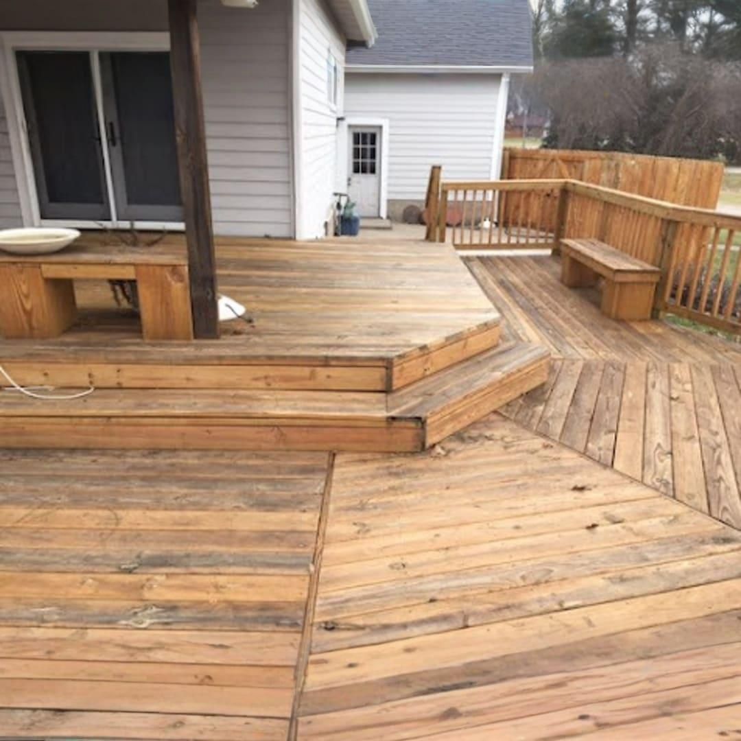 A multi-level wooden deck attached to a house with built-in benches, railings, and varying plank patterns.