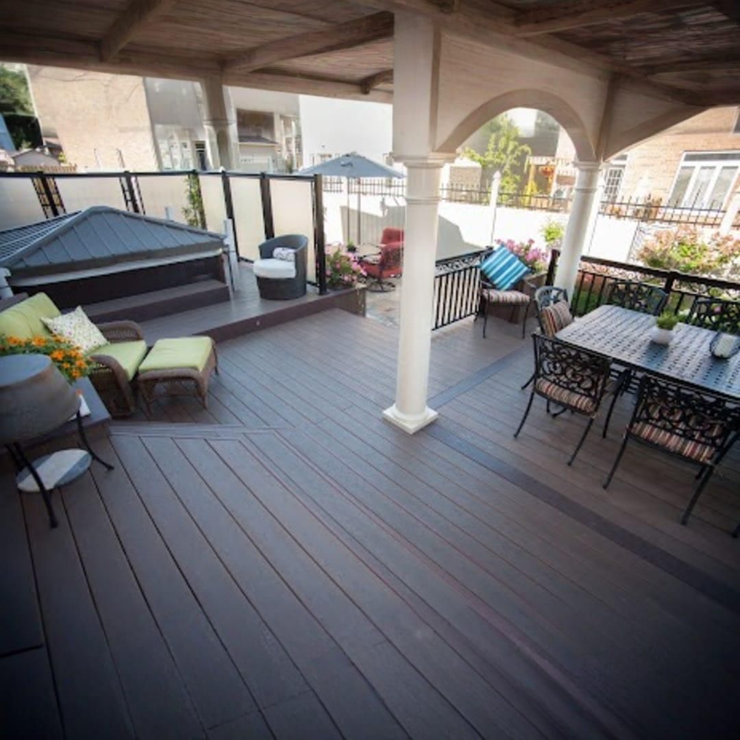 A spacious, multi-level deck featuring a hot tub, lounge chairs, and an outdoor dining set under a covered patio.