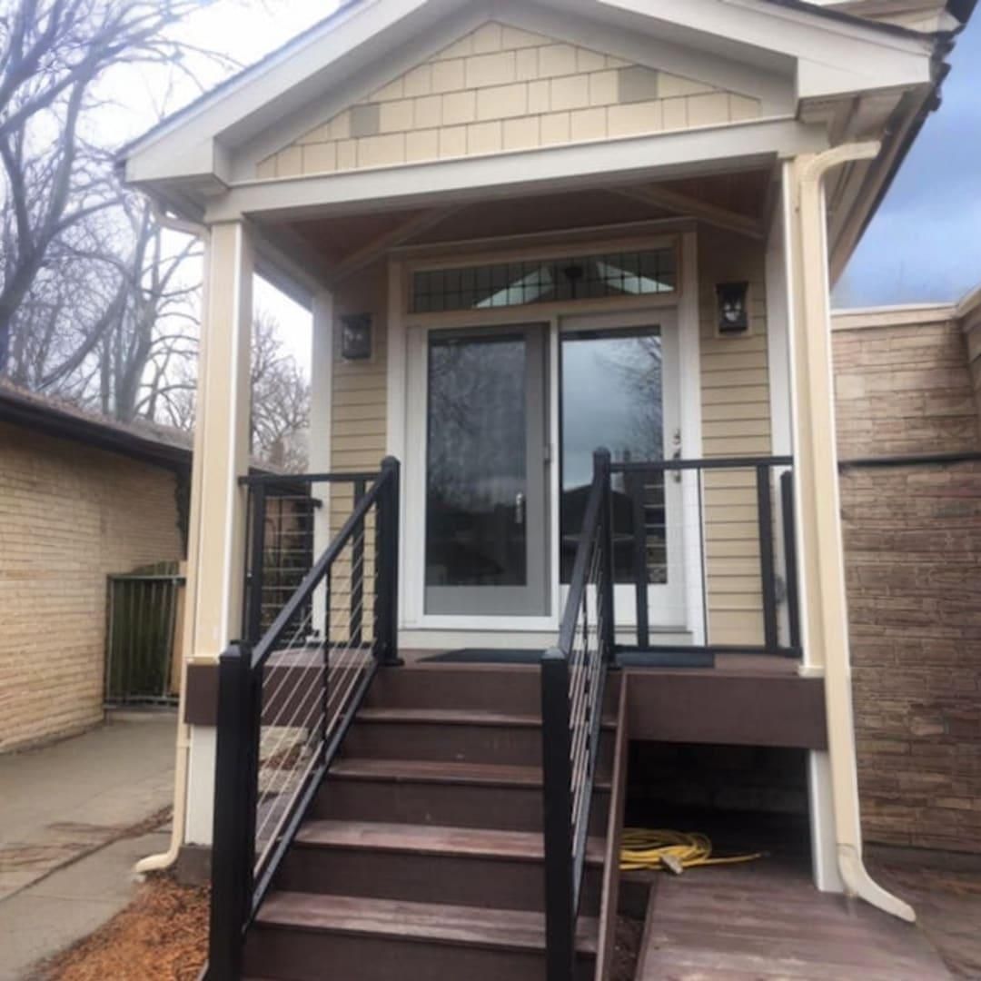 Front porch with steps, black railings, and a white door on a small beige house.