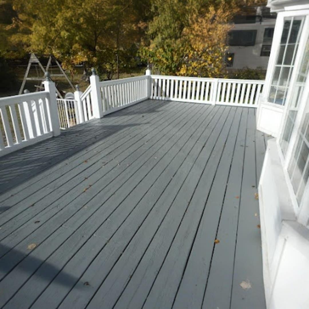 A gray wooden deck with white railings, looking out toward a backyard with trees and a play set.