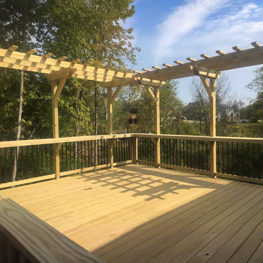 Wooden deck with pergola railing overlooking a green yard in warm sunlight