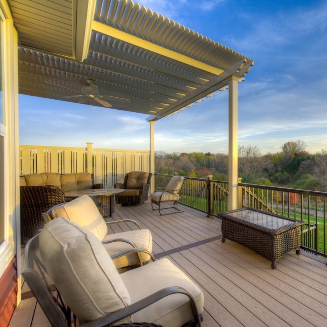 Covered wooden deck with cushioned chairs, pergola, and a view of trees and sky