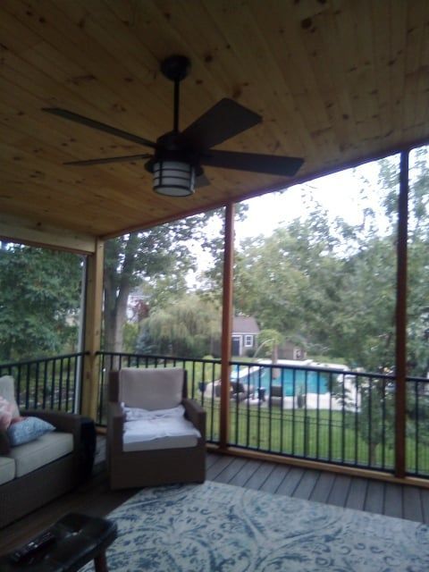 Covered porch with ceiling fan, seating, rug, and a view of a yard and pool through screened railings