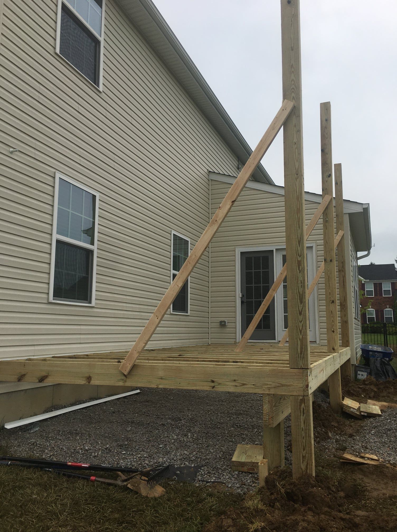 A wooden deck under construction is attached to the side of a tan vinyl-sided house, featuring several vertical posts.
