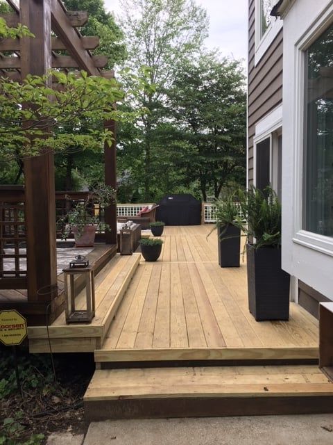 A wooden deck featuring a pergola, stairs, potted plants, and outdoor decor, viewed from a patio level.