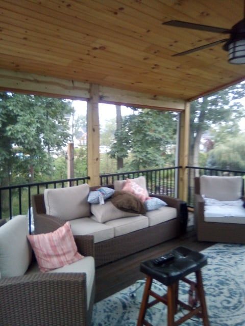 A cozy screened-in porch with outdoor wicker furniture, patterned cushions, a wooden ceiling, and a ceiling fan.