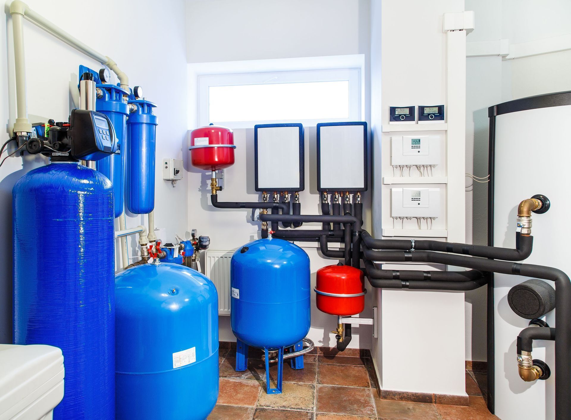 Blue water treatment system in a utility room. Pipes, tanks, and gauges against a white wall.