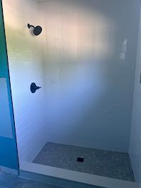 Modern shower with white walls, black fixtures, and a gray stone floor.