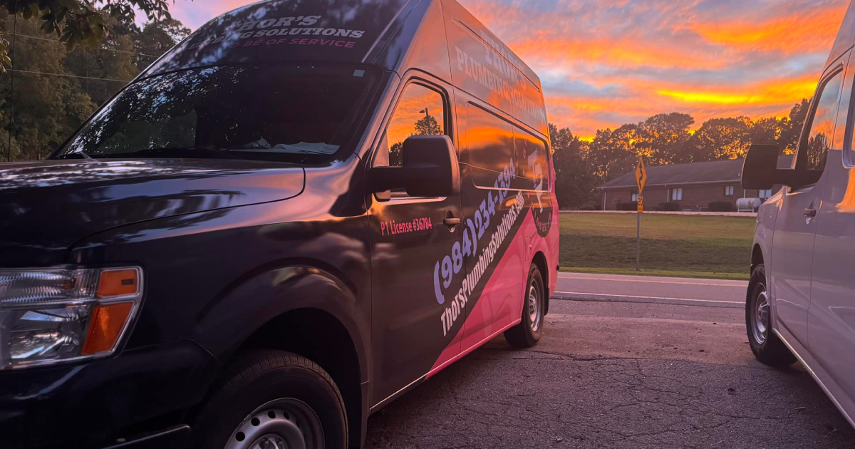 Two vans parked at dusk with a colorful sunset in the background. One van is black with pink graphics.