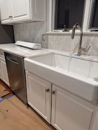 White farmhouse kitchen sink with running water, stainless steel dishwasher, and white cabinets.