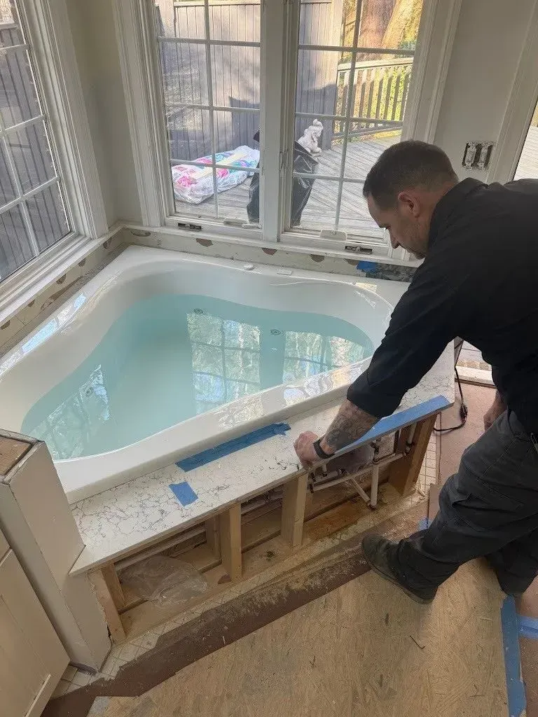 Person working on a bathtub surround in a bathroom with a window. The tub is filled with water.