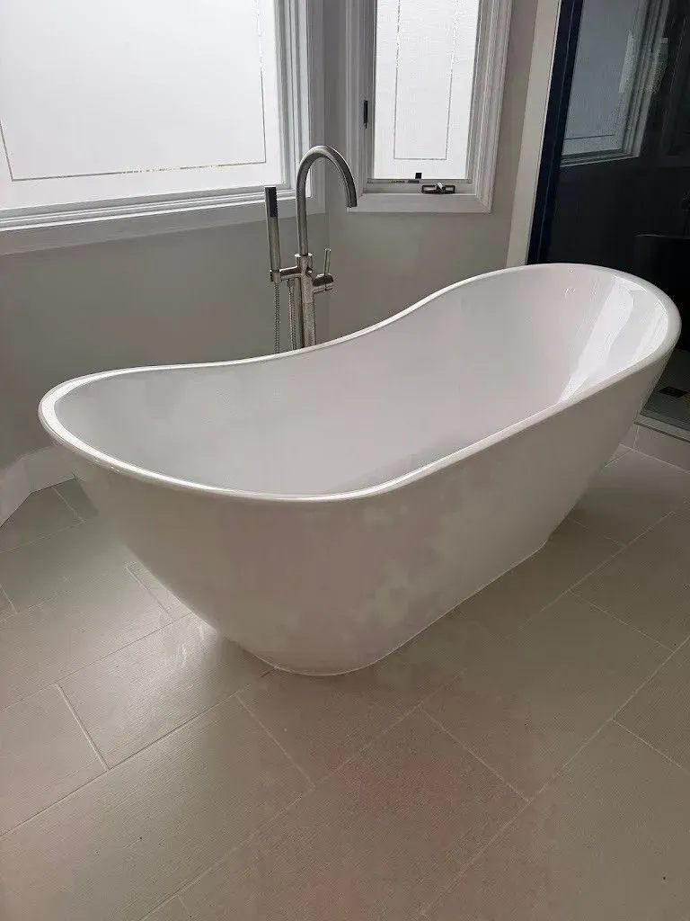White freestanding bathtub in a bathroom, near a window and faucet.
