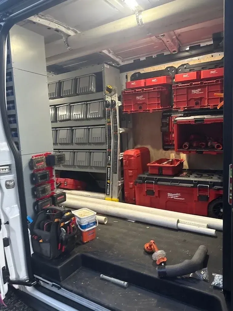 Interior of a work van with organized storage, including bins, red toolboxes, and a ladder.
