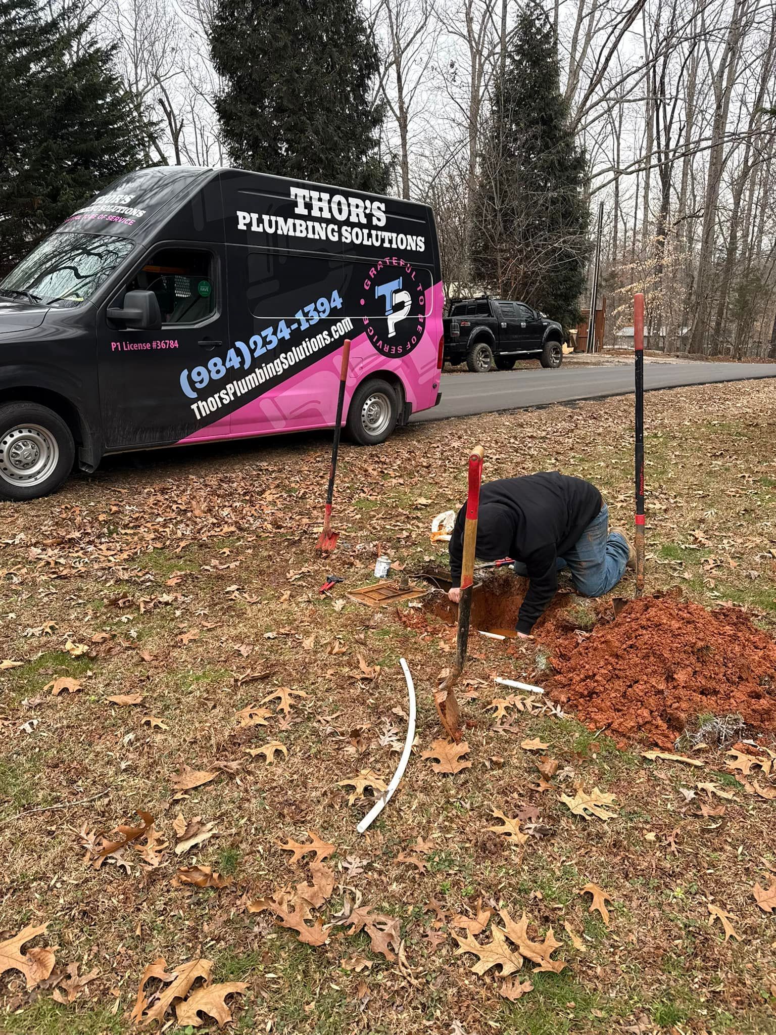 Plumber working outside near a van, digging in a yard with white pipe visible.