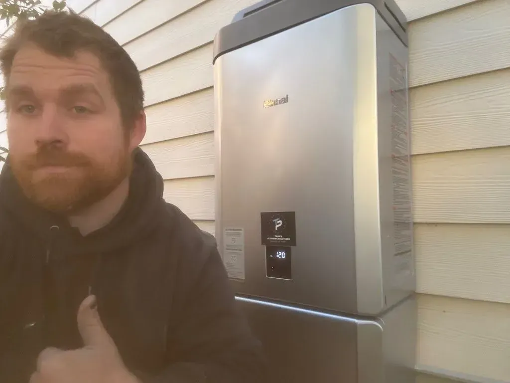Man gives thumbs up next to a silver solar panel battery mounted on a beige house siding.