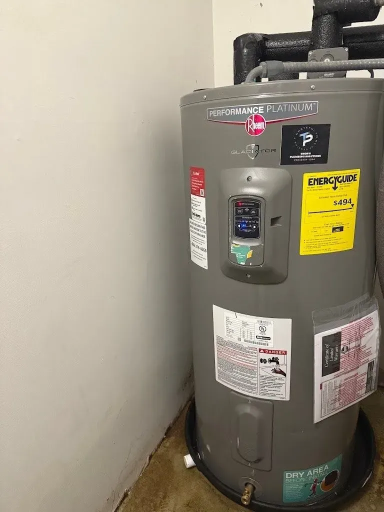 A Rheem water heater in a utility room. Gray tank with control panel and attached labels.