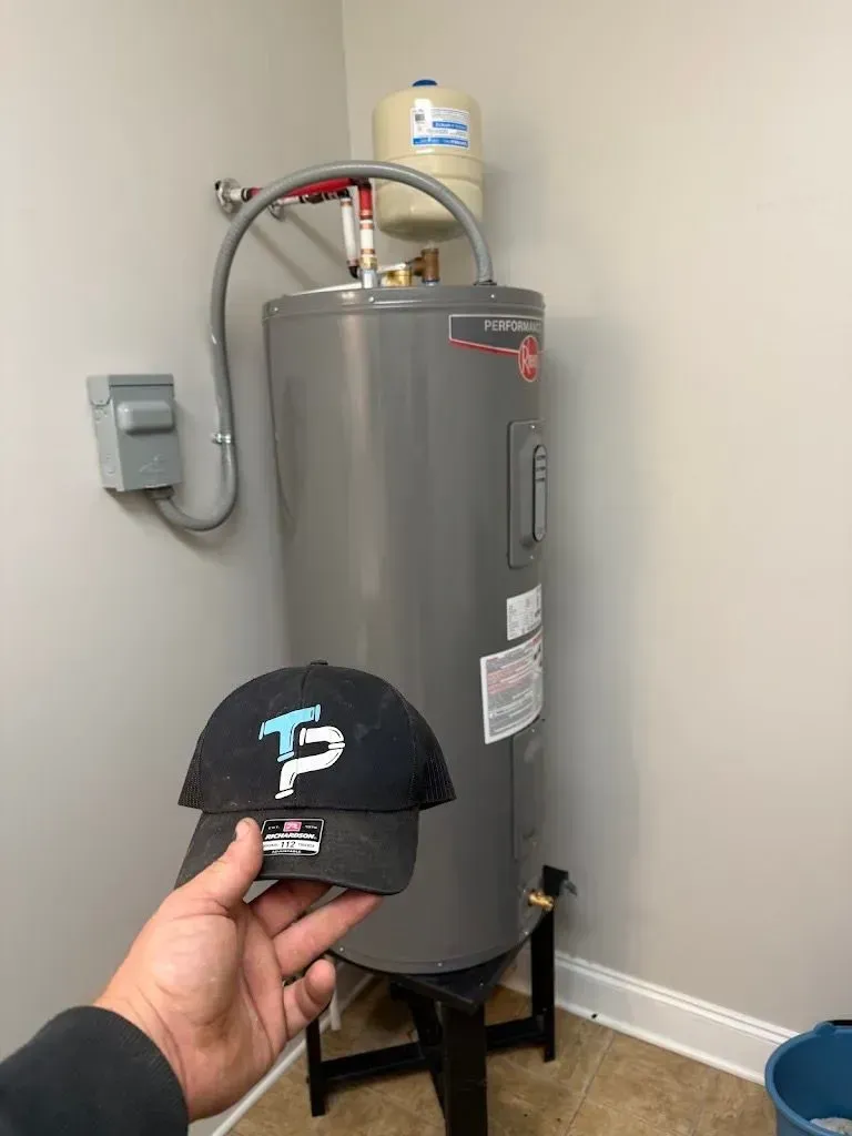 Hand holding a black cap in front of a water heater with expansion tank in a utility room.