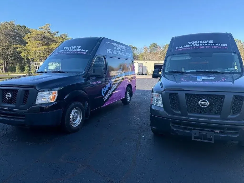 Two black Nissan vans with business logos parked on pavement. One van has purple accents.