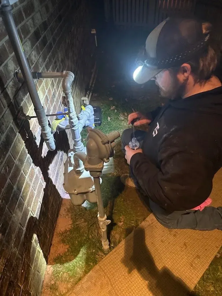 Two people working on gas meter outside brick building at night; one wearing headlamp.