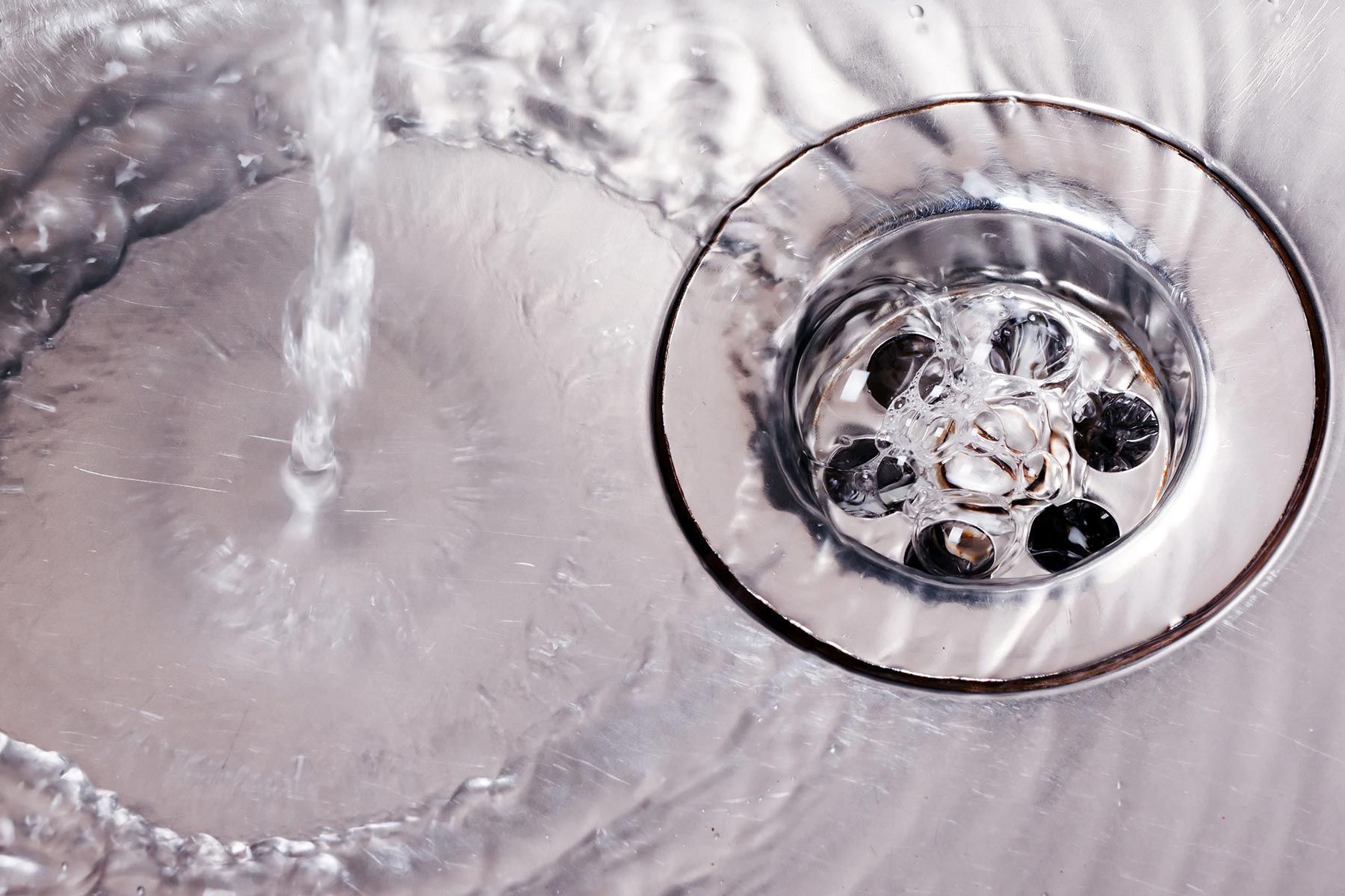 Water flowing into a shiny, stainless steel sink drain.