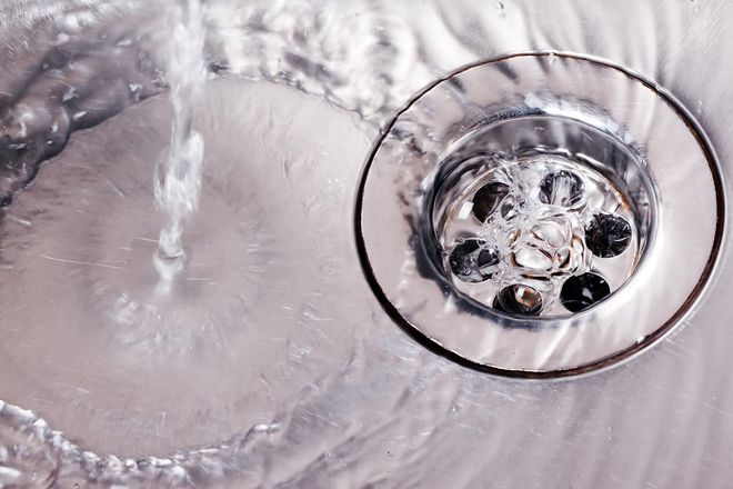 Water flowing into a shiny, stainless steel sink drain.