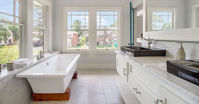 Spacious white bathroom with a freestanding tub, bright windows, and a long countertop.