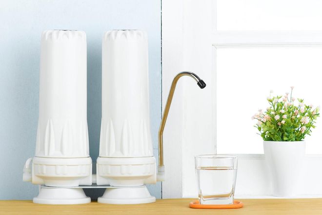 Water filter system with a glass of water, a plant, and a window.