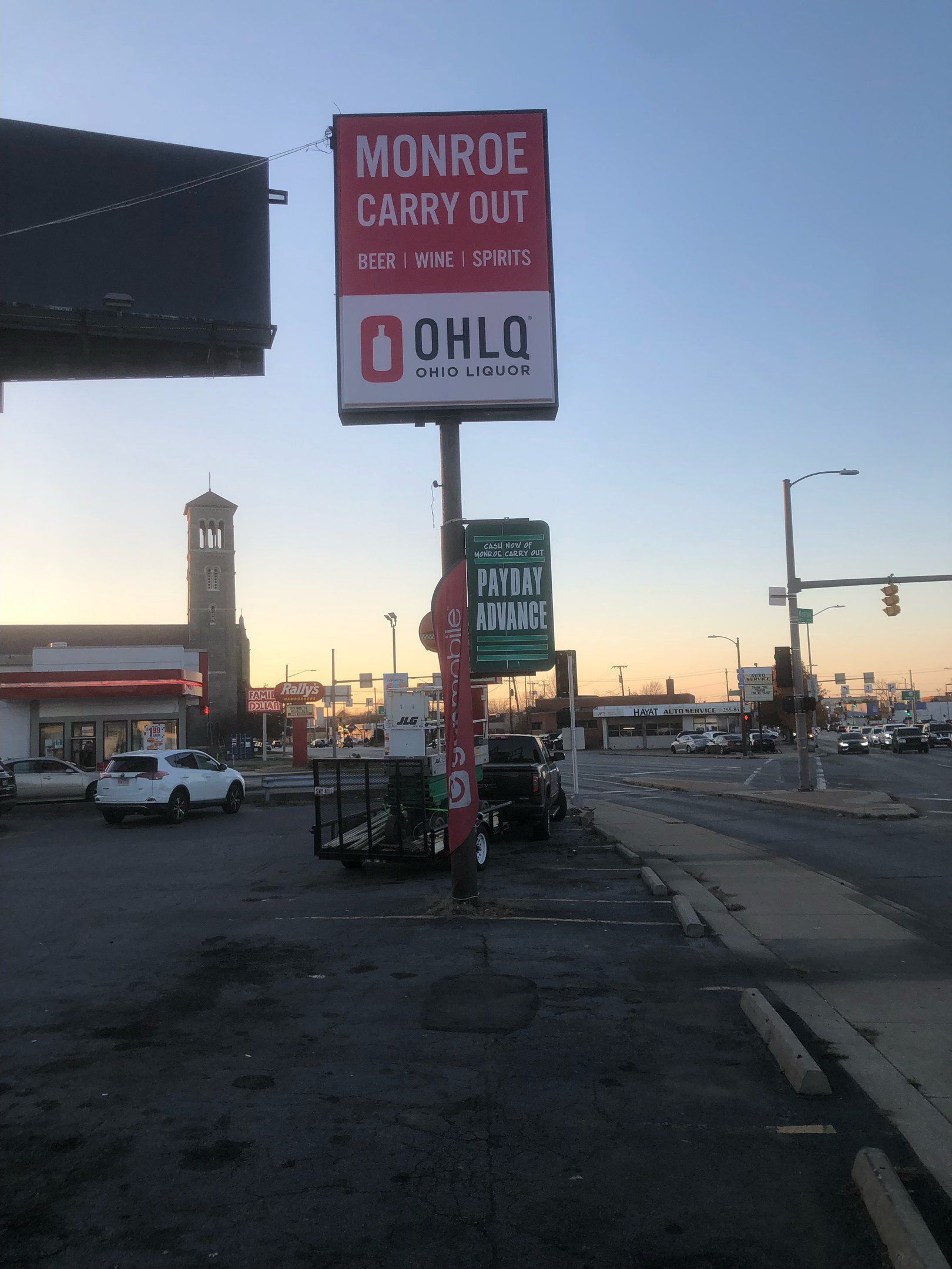 Sign for Monroe Carry Out and Ohio Liquor store. Roadside view with parked cars, and a tower building in the background.