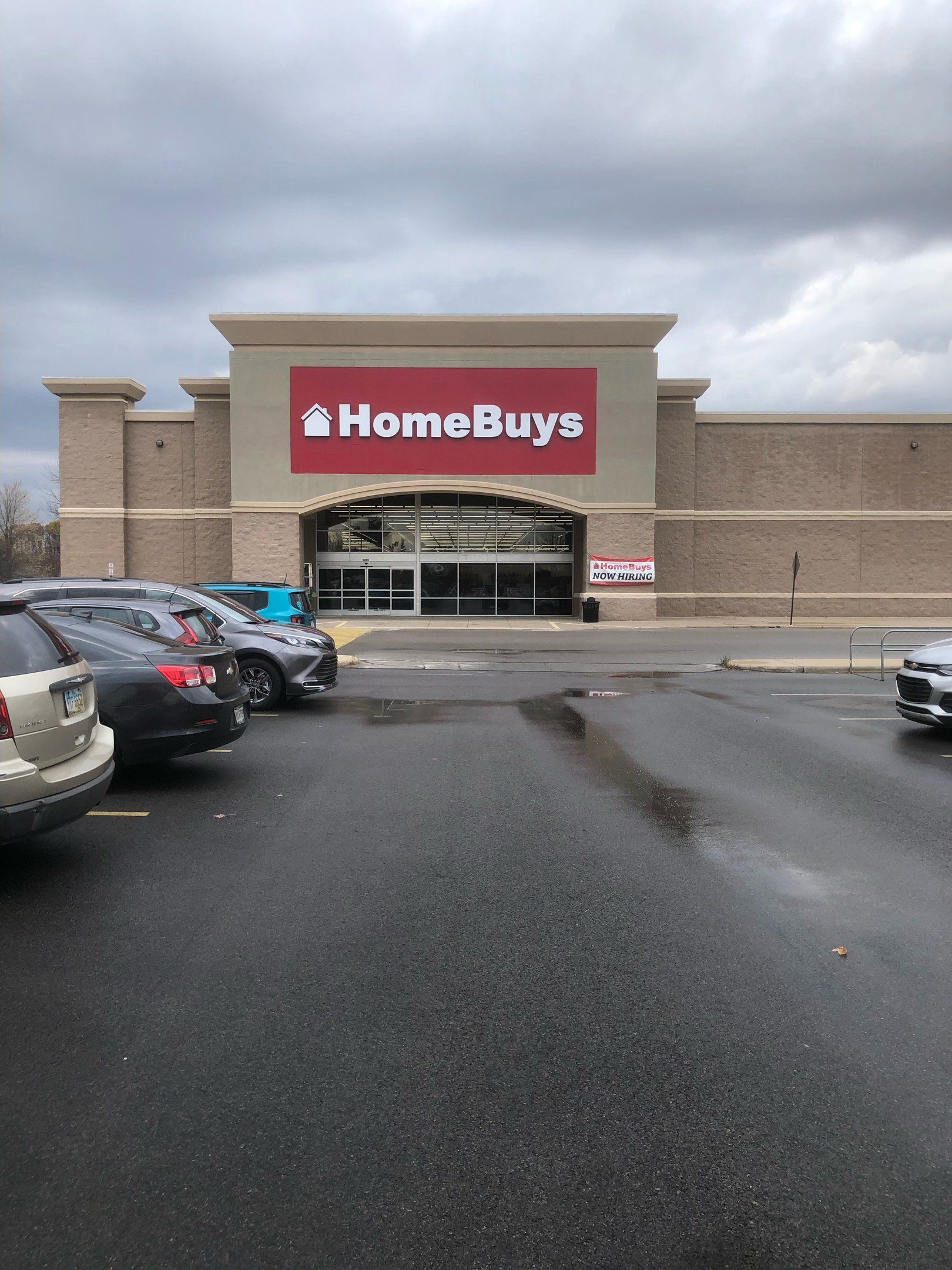 HomeBuys store exterior, red sign, cars in parking lot, cloudy sky.