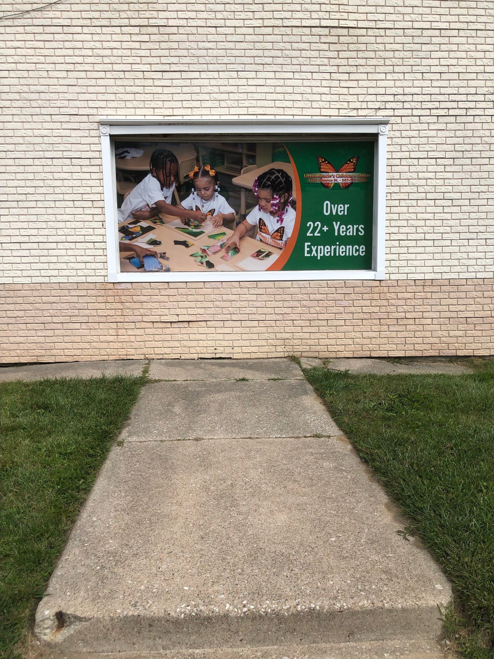 A concrete path leads to a brick building with a window displaying a childcare advertisement.