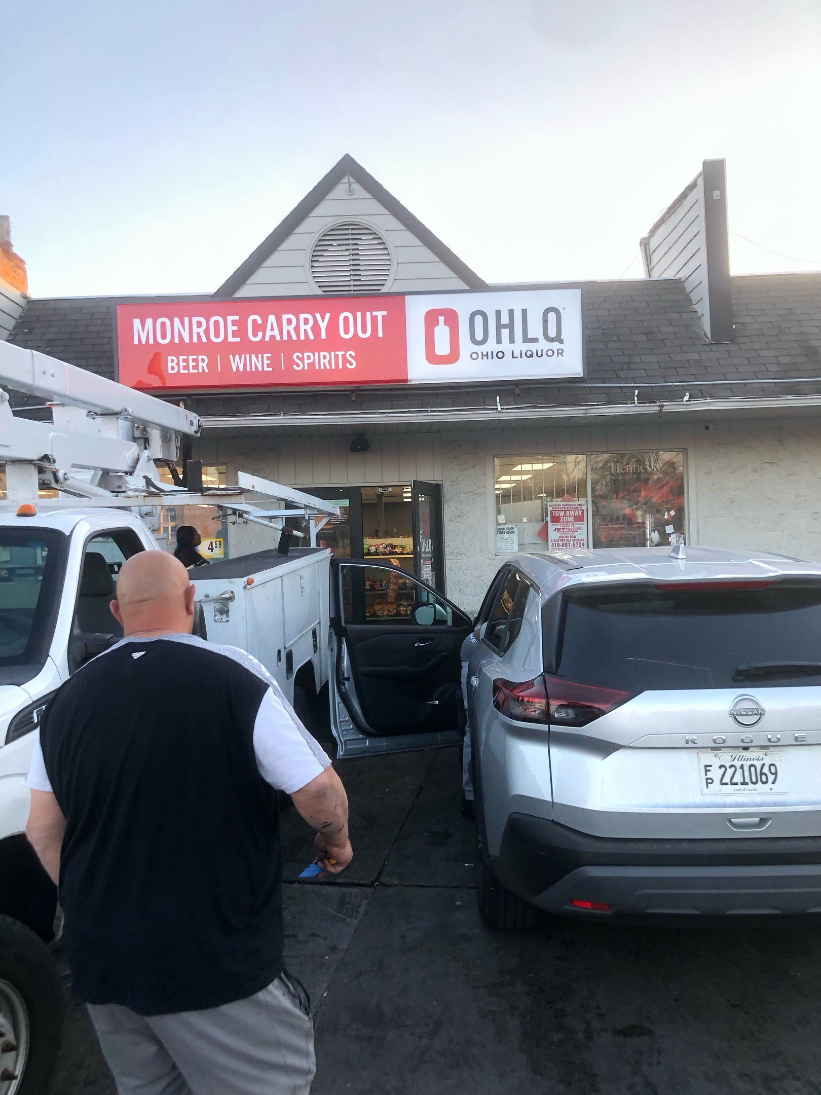 A man stands near a silver SUV and white work truck, both damaged in front of Monroe Carry Out in Ohio.