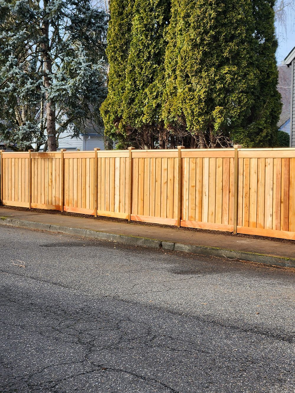 A wooden fence is sitting on the side of a road next to a tree