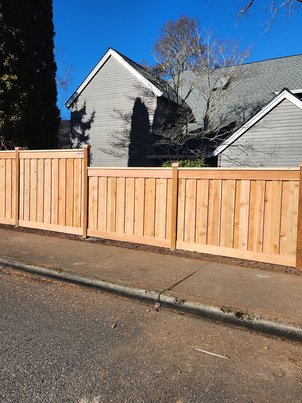A wooden fence is sitting on the side of the road in front of a house