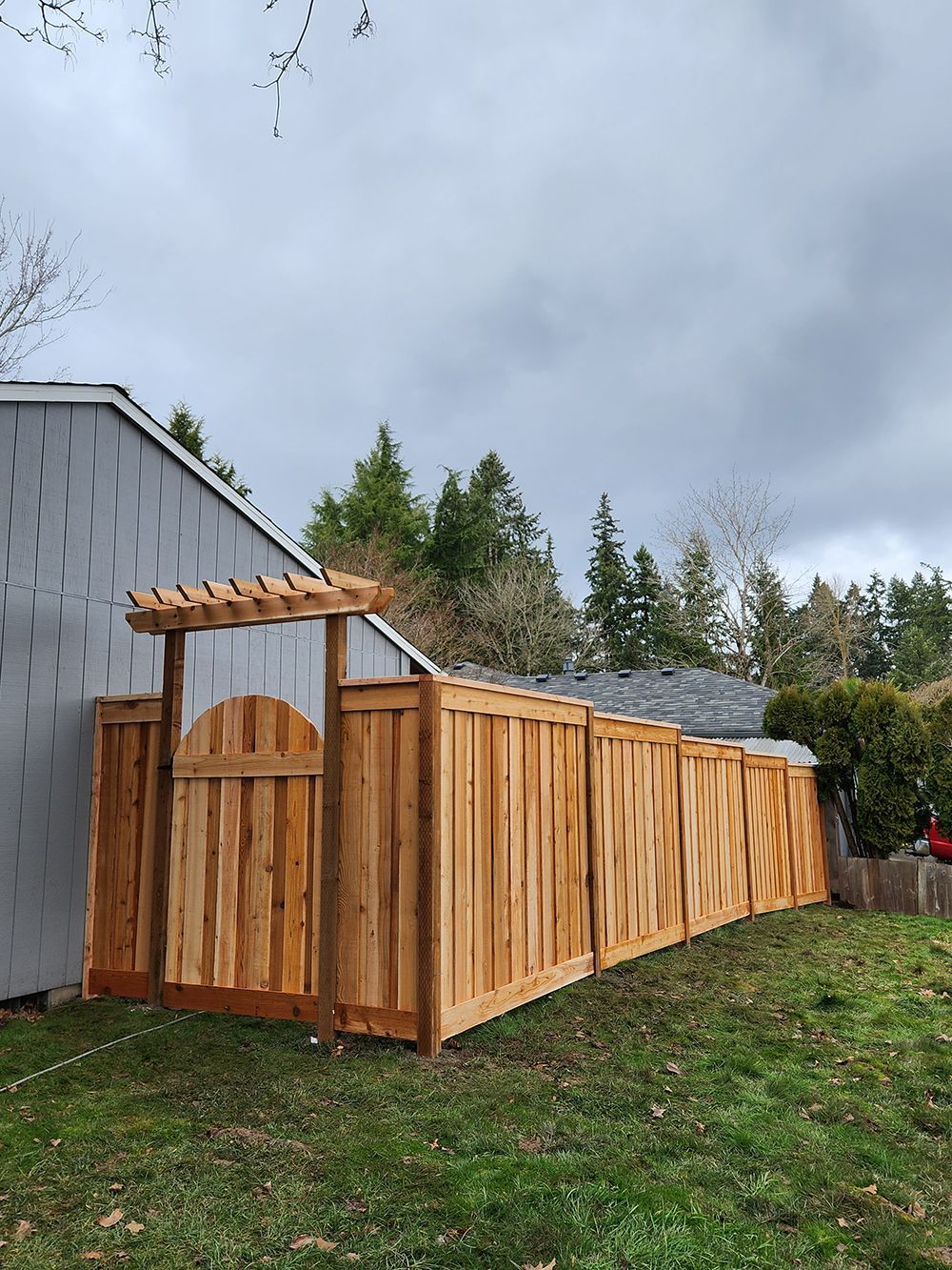 A wooden fence with a gate and pergola in front of a house