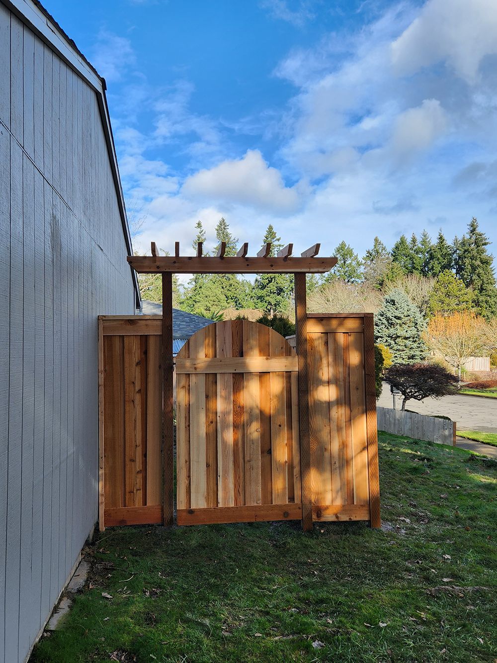 A wooden gate with a pergola attached to it is in the backyard of a house