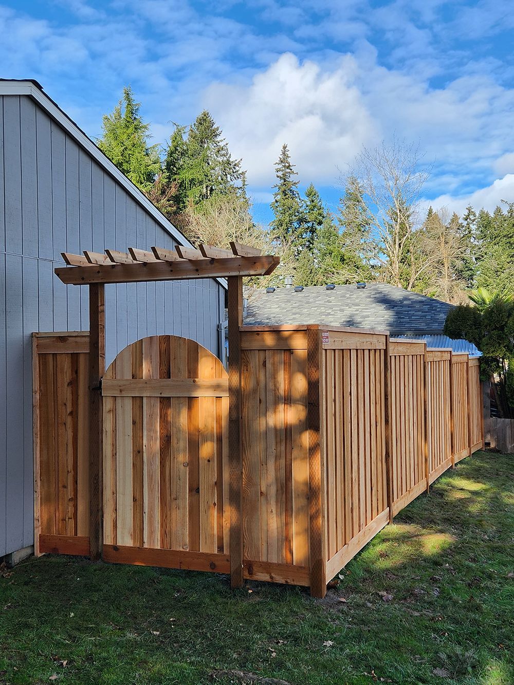 A wooden fence with a gate and pergola in front of a house
