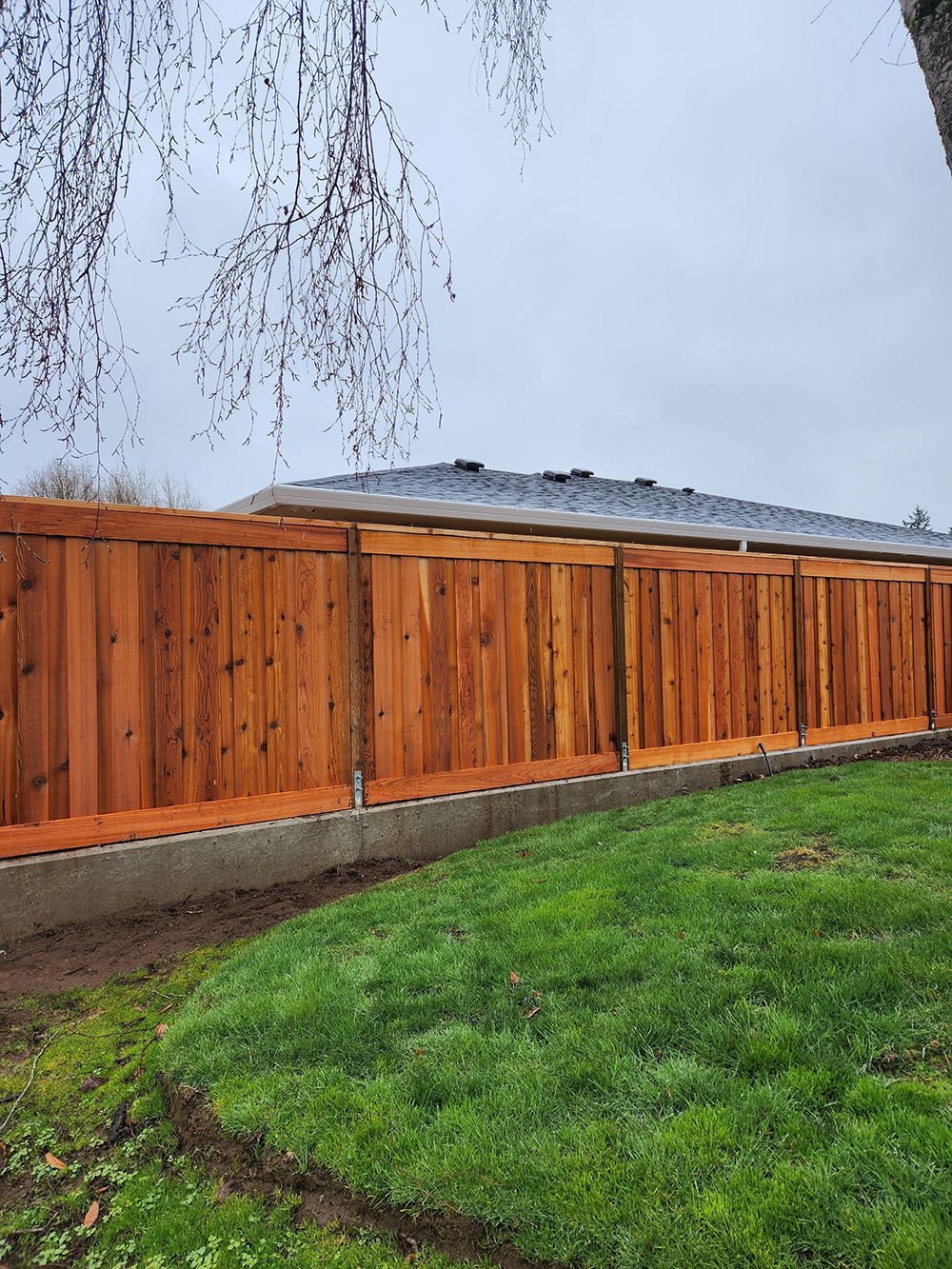 A wooden fence surrounds a lush green lawn in front of a house