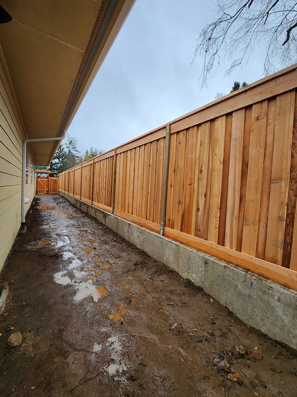 A wooden fence is surrounding a dirt path next to a house