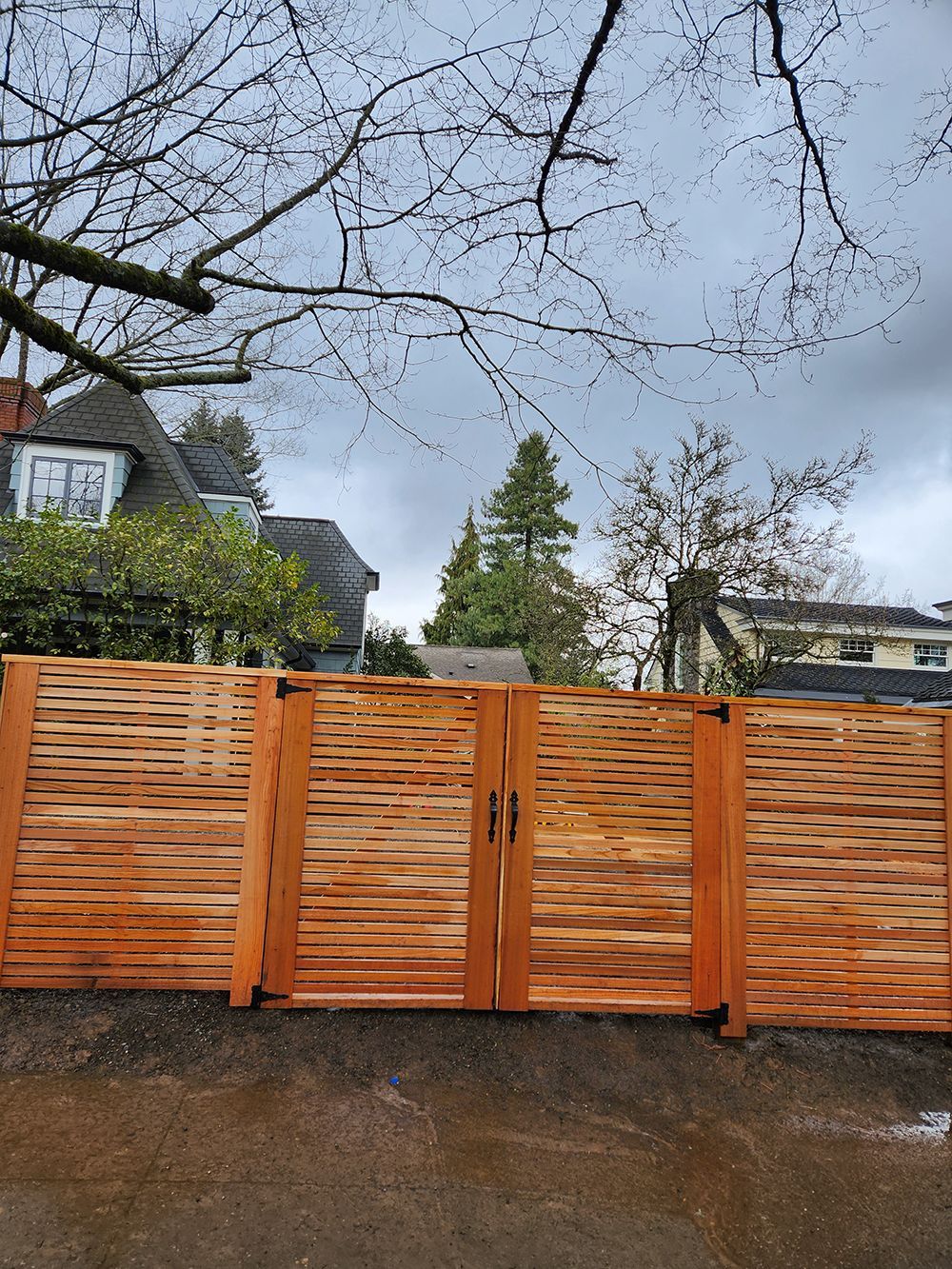 A wooden fence with a gate in front of a house on a cloudy day