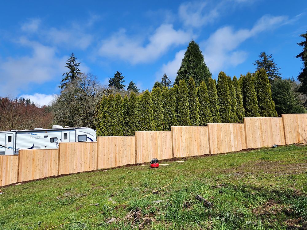 A wooden fence surrounds a grassy field with a trailer in the background