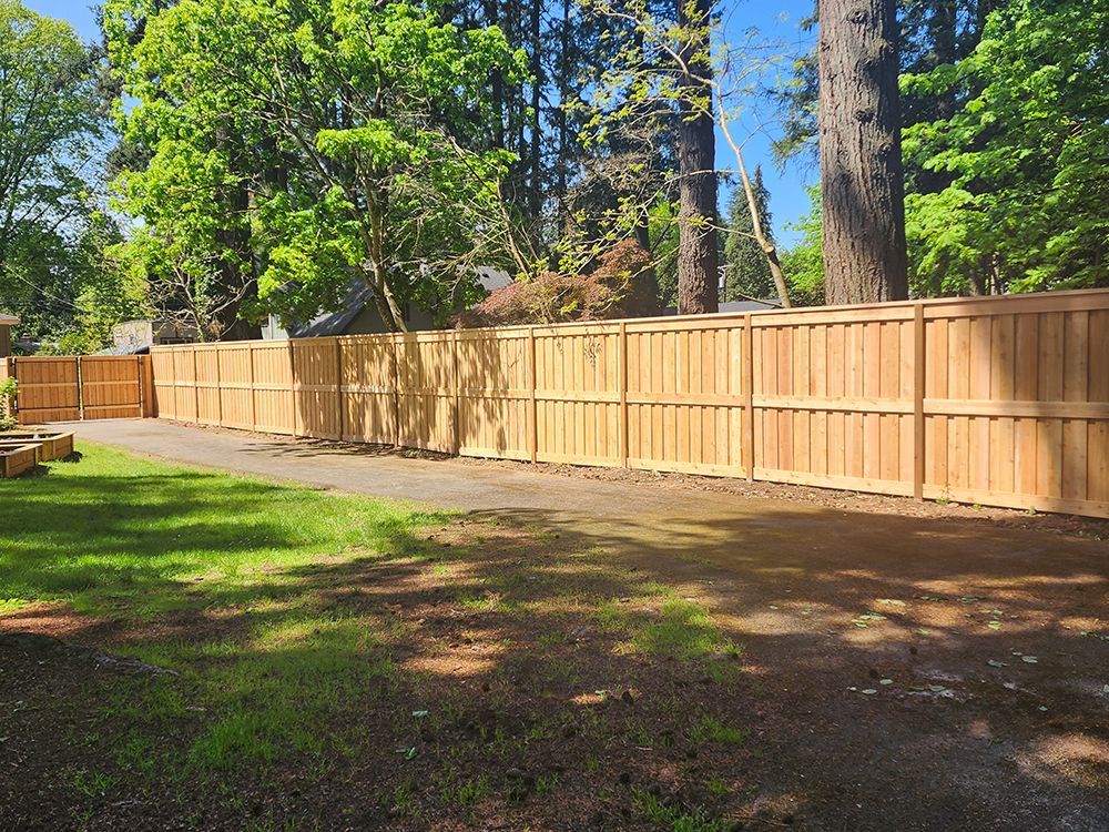 A wooden fence surrounds a lush green yard with trees in the background