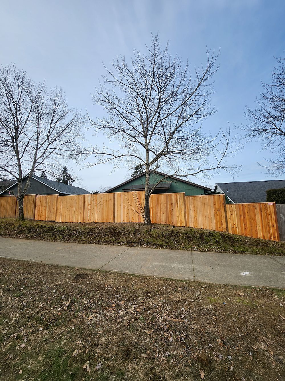 A wooden fence is sitting next to a sidewalk in front of a house