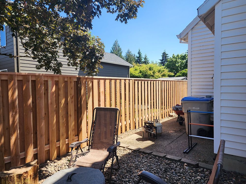 A wooden fence surrounds a backyard with a chair in front of it