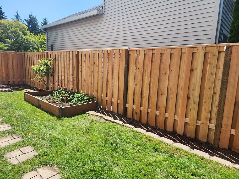 A wooden fence surrounds a garden in a backyard