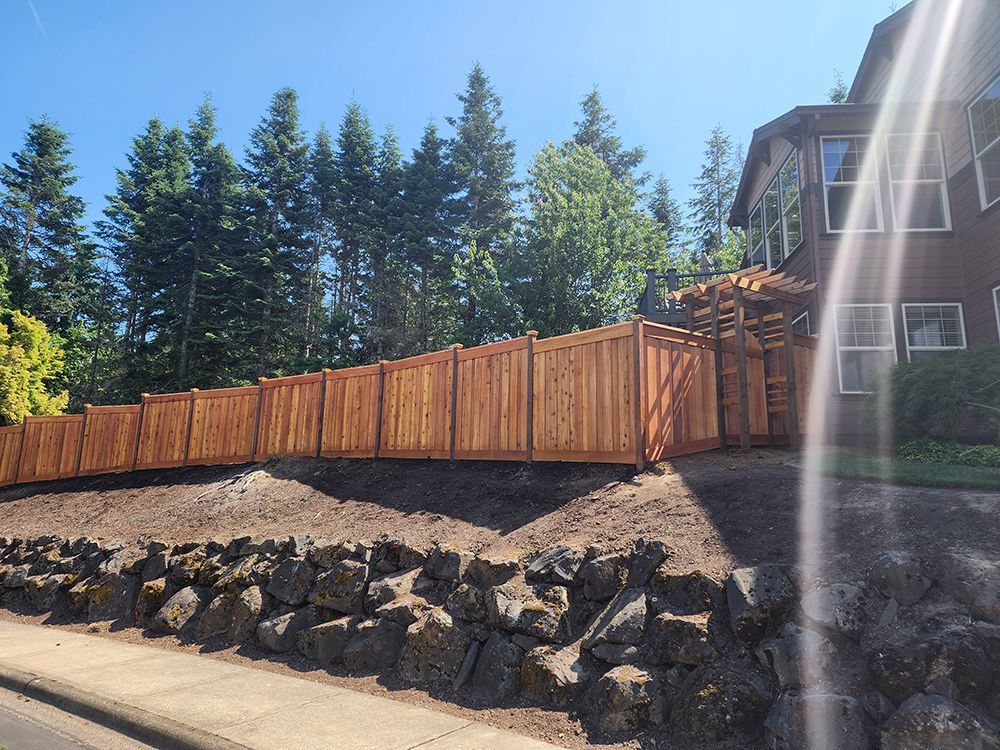 A wooden fence is surrounded by rocks and trees in front of a house